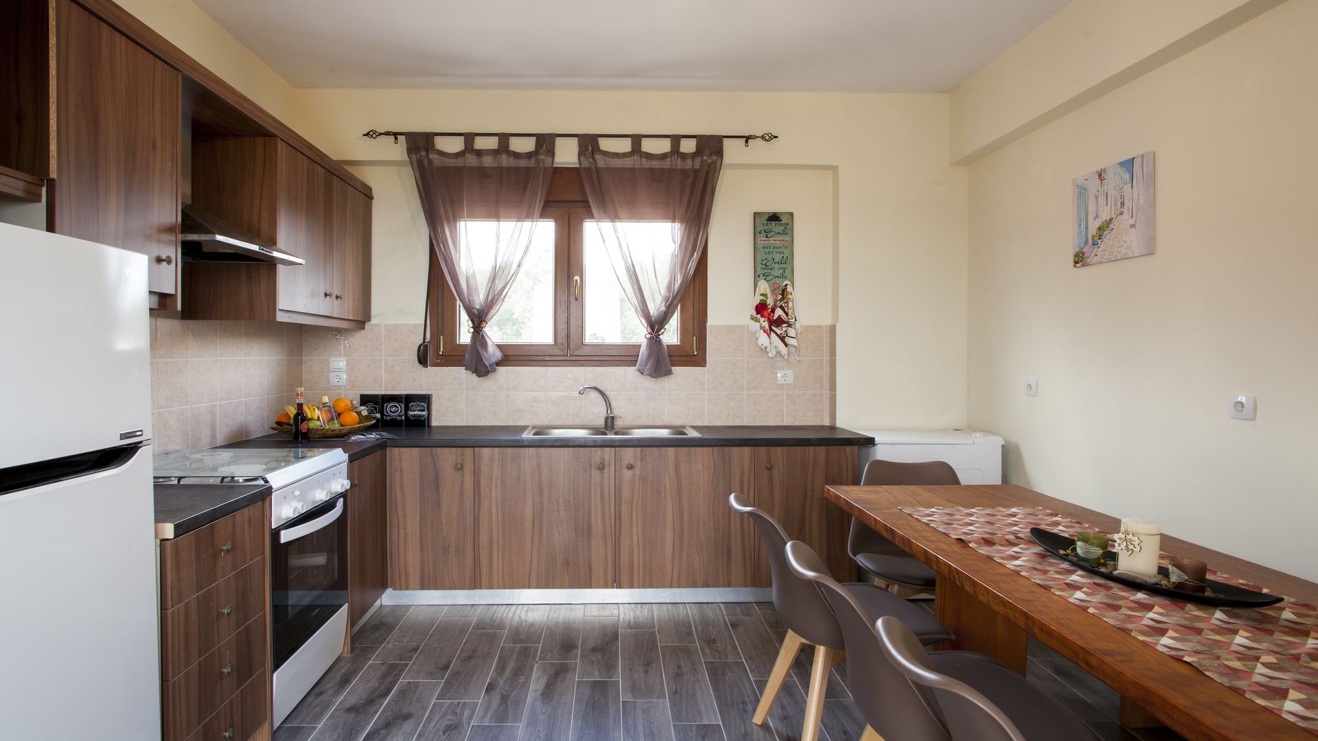 Una cocina compacta con armarios de madera, horno empotrado, lavamanos y una zona de comedor con mesa y sillas.