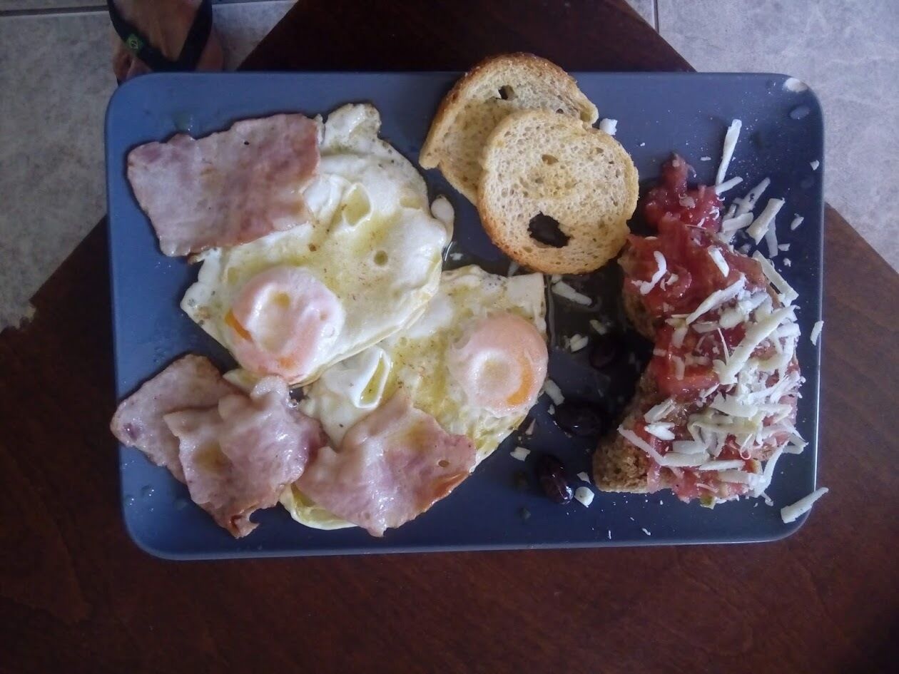 Une assiette de petit-déjeuner avec des œufs, du bacon, des toasts et de la sauce tomate.