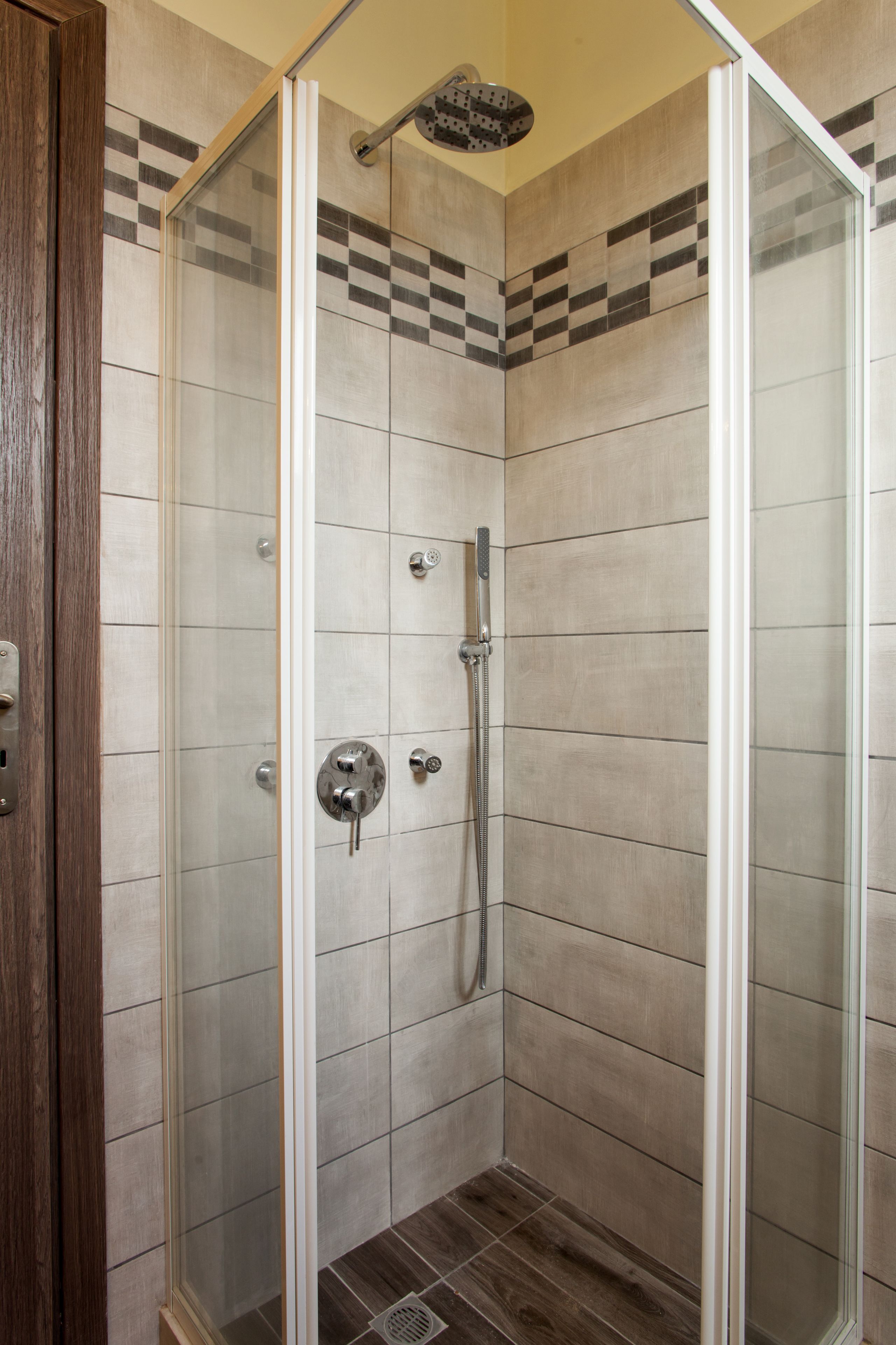Une douche à l’italienne avec une porte en verre, des murs carrelés et un pommeau de douche.