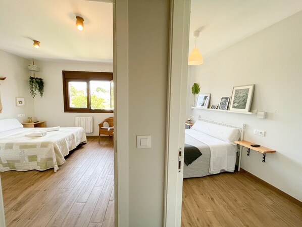 A bedroom with two beds, wooden flooring, a window, a radiator, and a hanging plant. - Villa Galicia (Caldas de Reis)