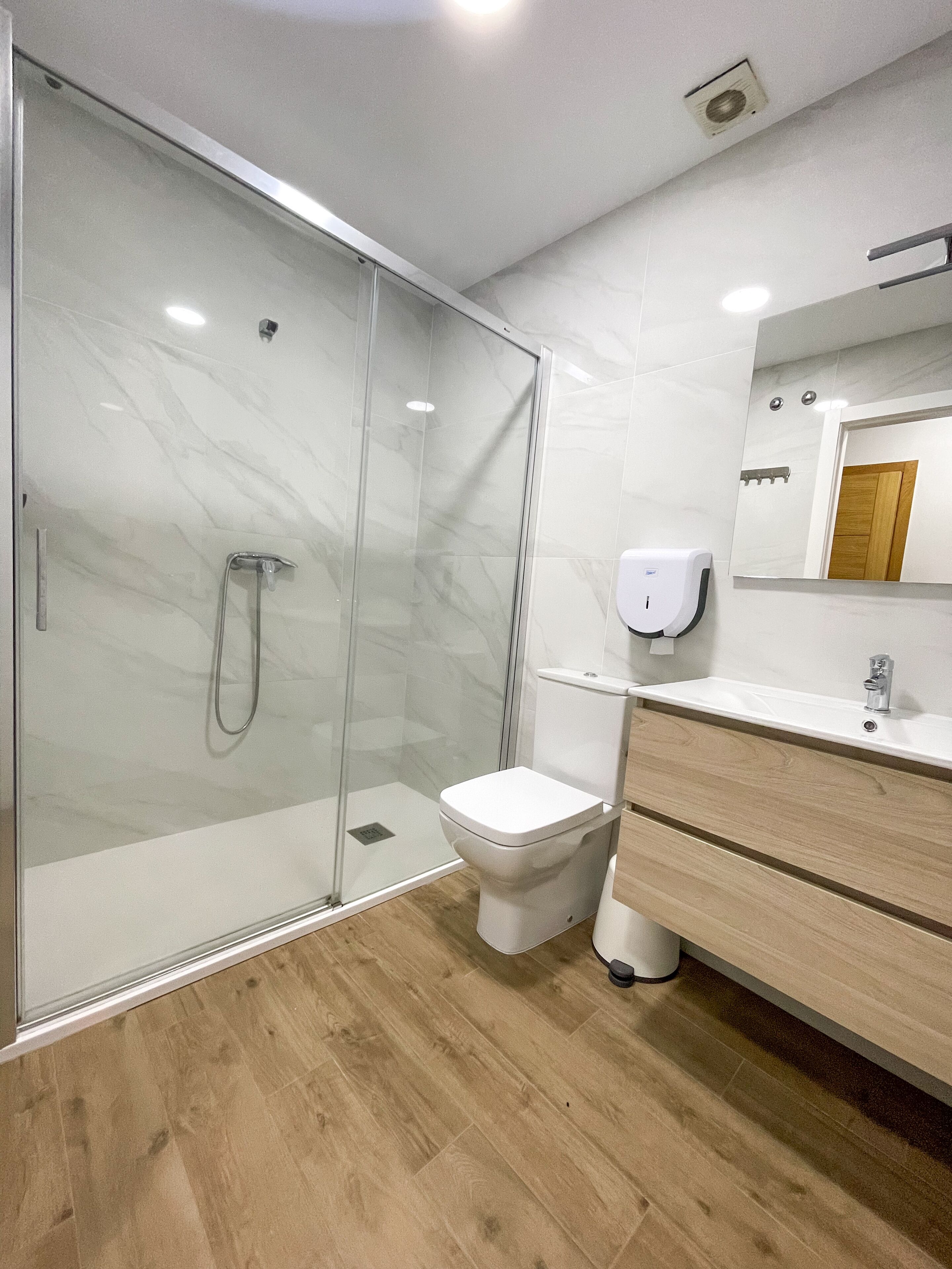 Un baño moderno con ducha de vidrio, inodoro y tocador con espejo.