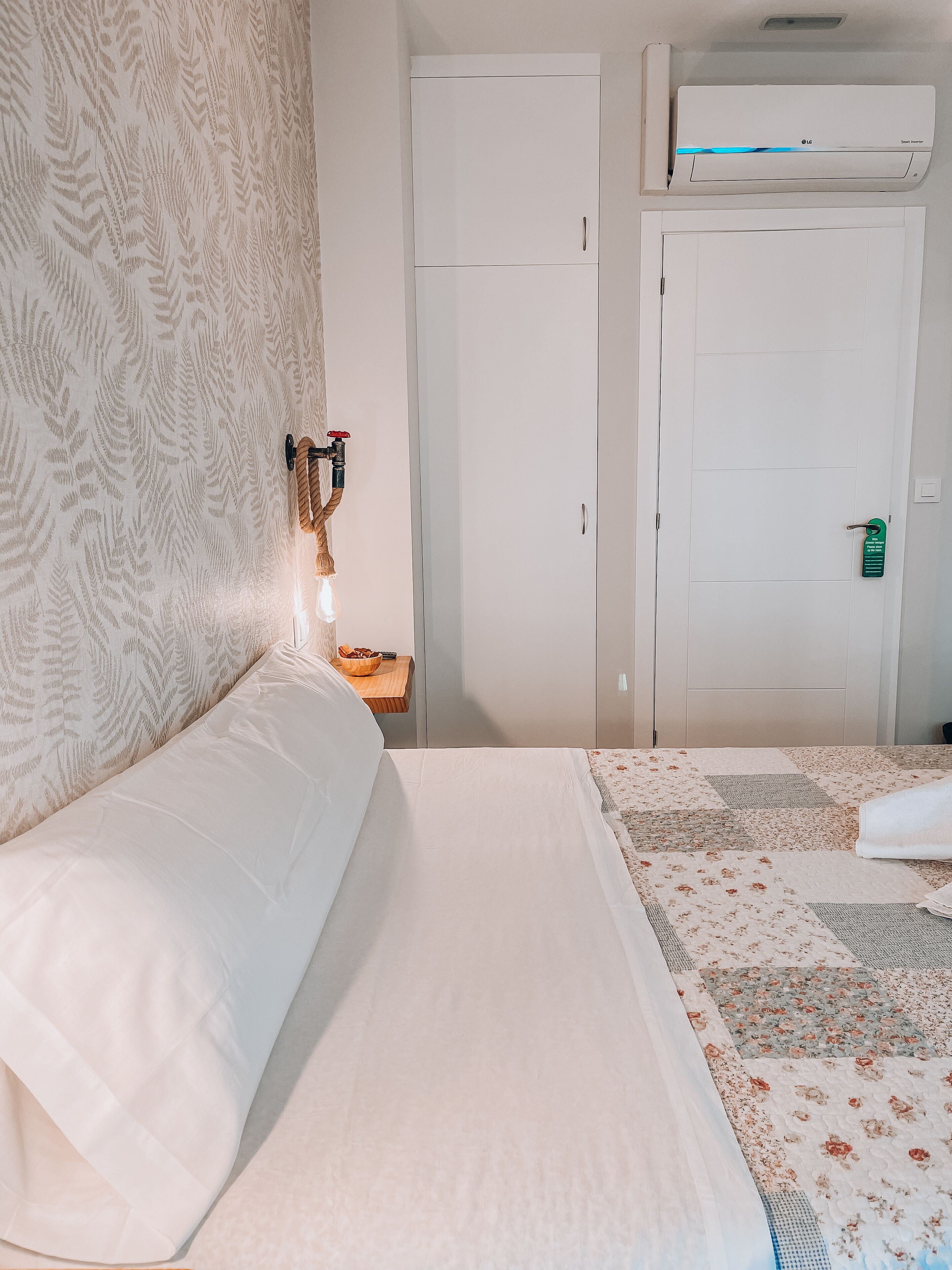 Una habitación de hotel con cama, mesita de noche, calentador de pared y armario.