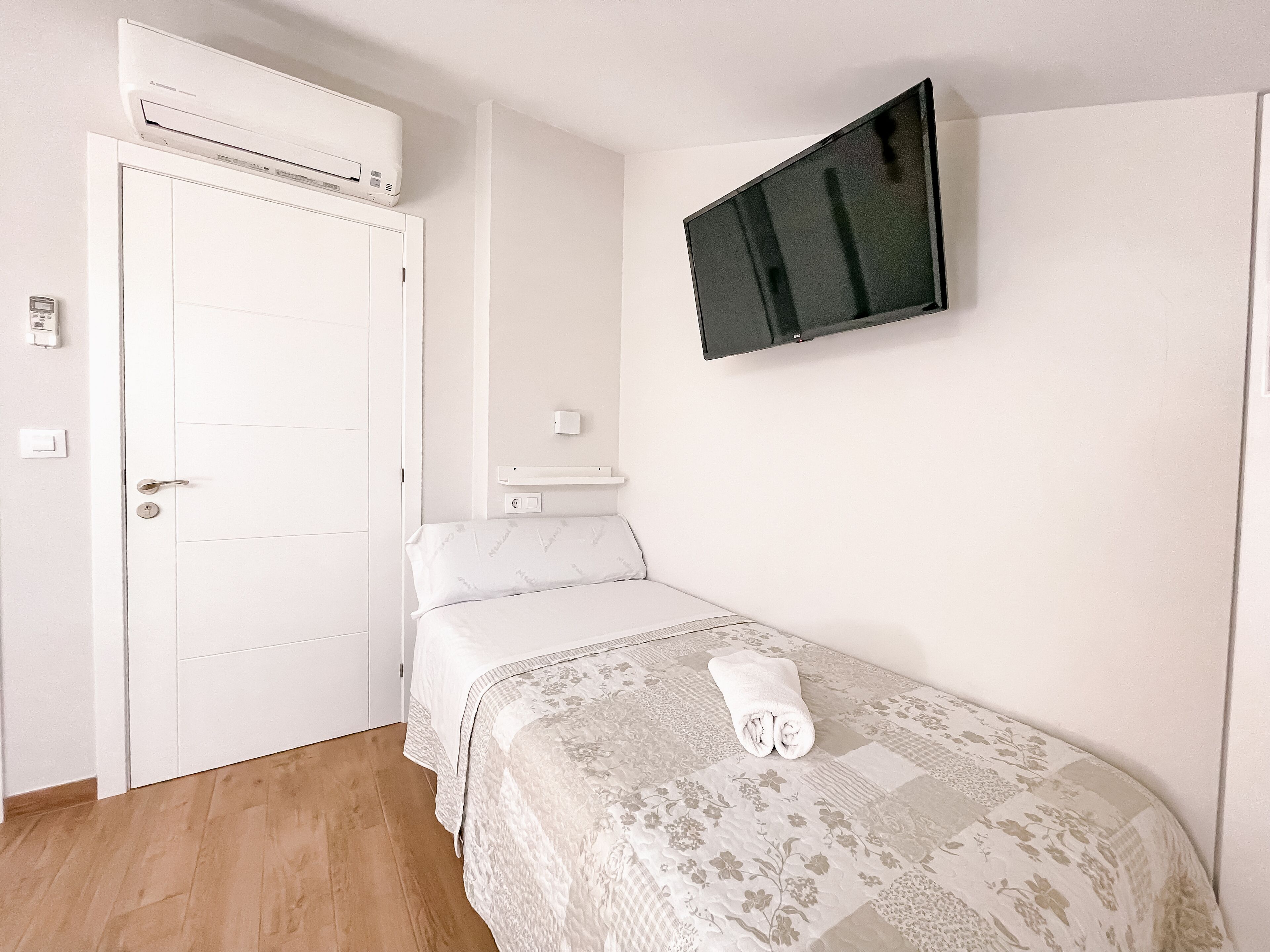 Une chambre à coucher comprenant un lit, un téléviseur fixé au mur, un appareil de climatisation et une porte.