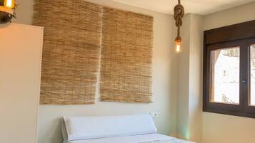 Un dormitorio con una cama, una silla de mimbre, una lámpara colgante y una ventana con vistas.