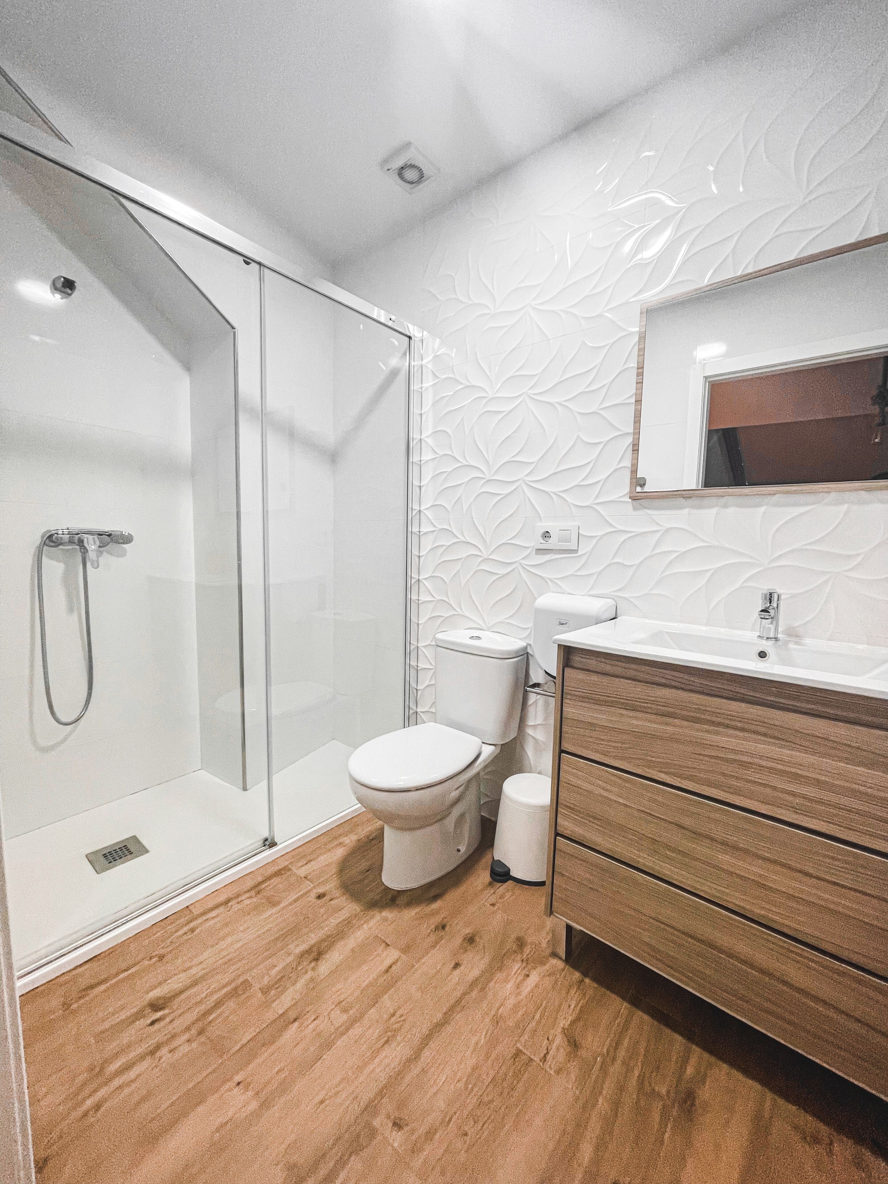 Ein modernes Badezimmer mit Duschkabine aus Glas, Toilette und einem Holzausleger mit Spiegel.