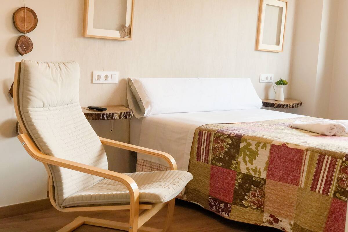 Une chambre d’hôtel avec un lit, une chaise, une petite table et un miroir fixé au mur.