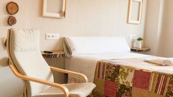 A hotel room with a bed, a chair, a small table, and a wall-mounted mirror.