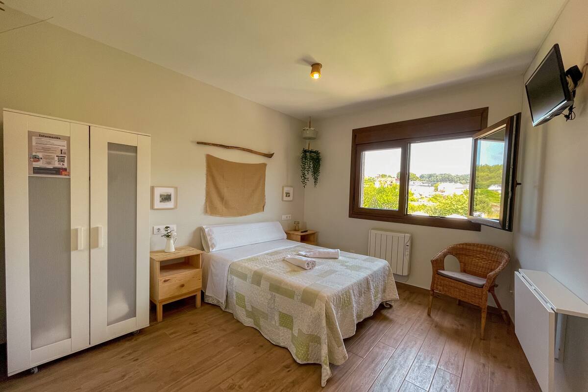Une chambre à coucher avec un lit, une armoire, une fenêtre donnant sur un beau paysage, une chaise et un téléviseur fixé au mur.
