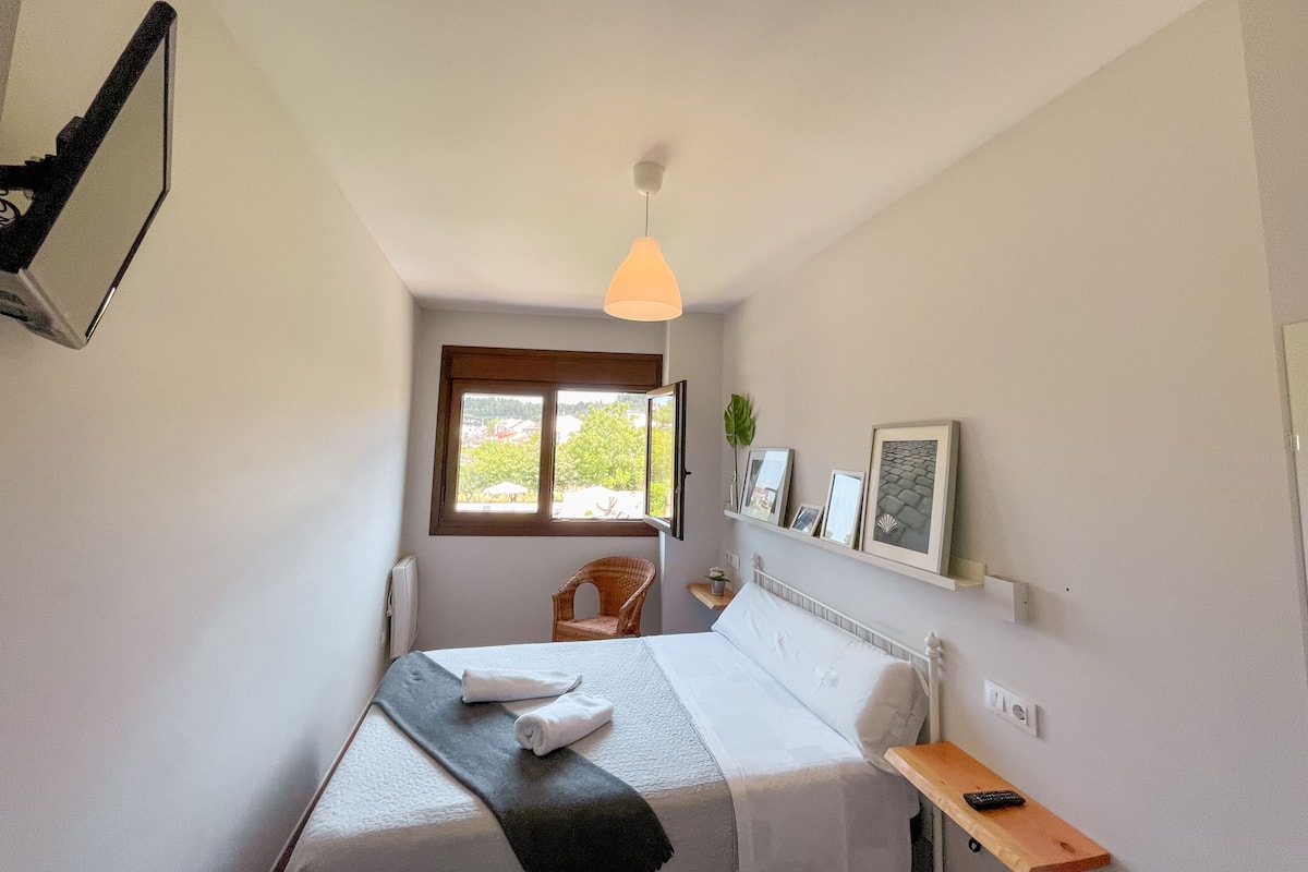 Une chambre à coucher avec un lit, une fenêtre, une chaise, une étagère avec des photos et une table de chevet.