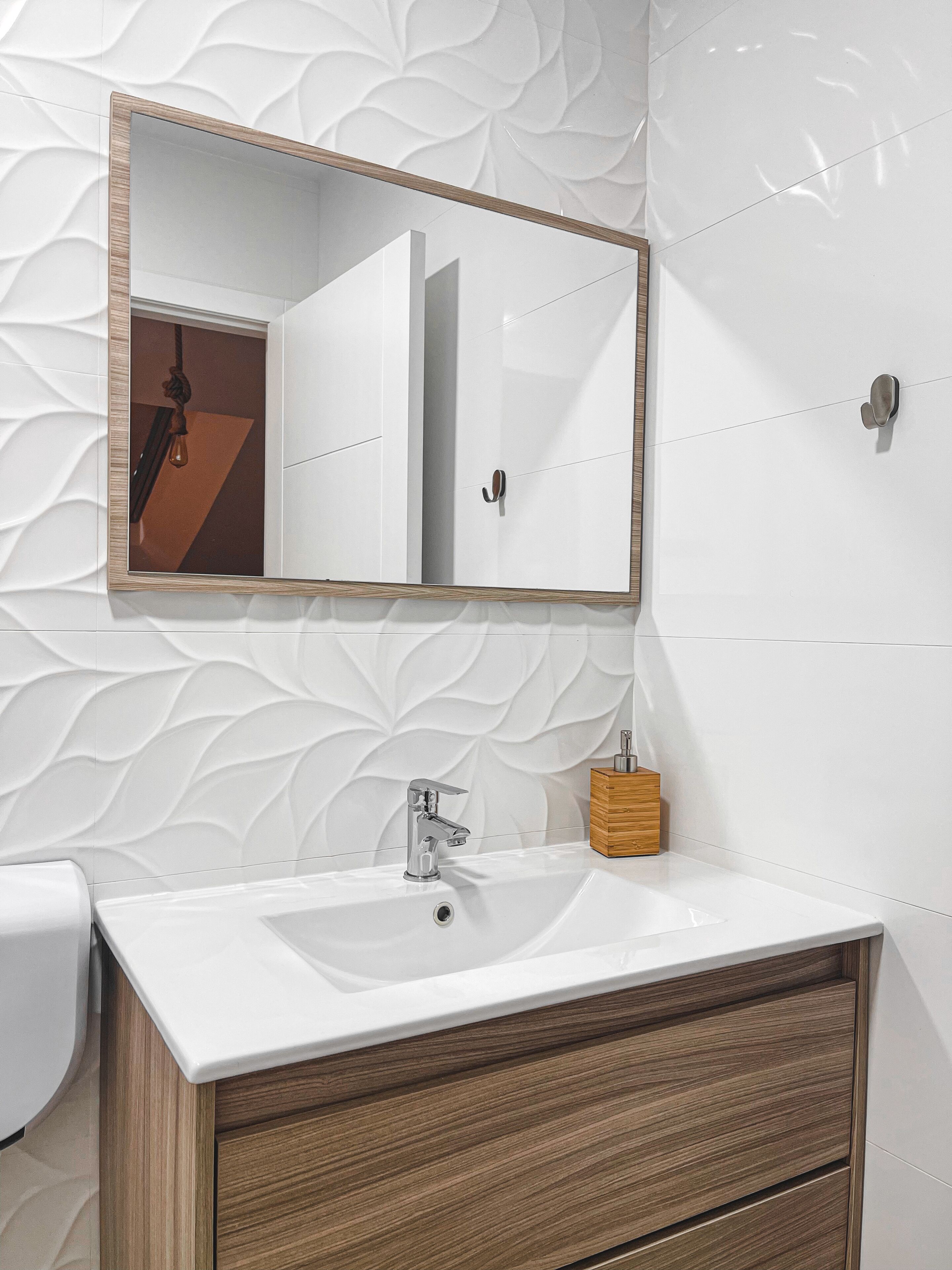 Ein Badezimmer mit einem weißen Waschbecken, einem Holz-Waschtisch und einem Spiegel mit Holzrahmen.