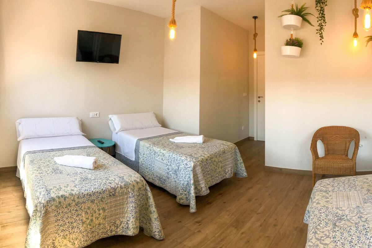 Une chambre d’hôtel avec deux lits simples, un canapé-lit, une petite table, une chaise, une armoire et un téléviseur fixé au mur.