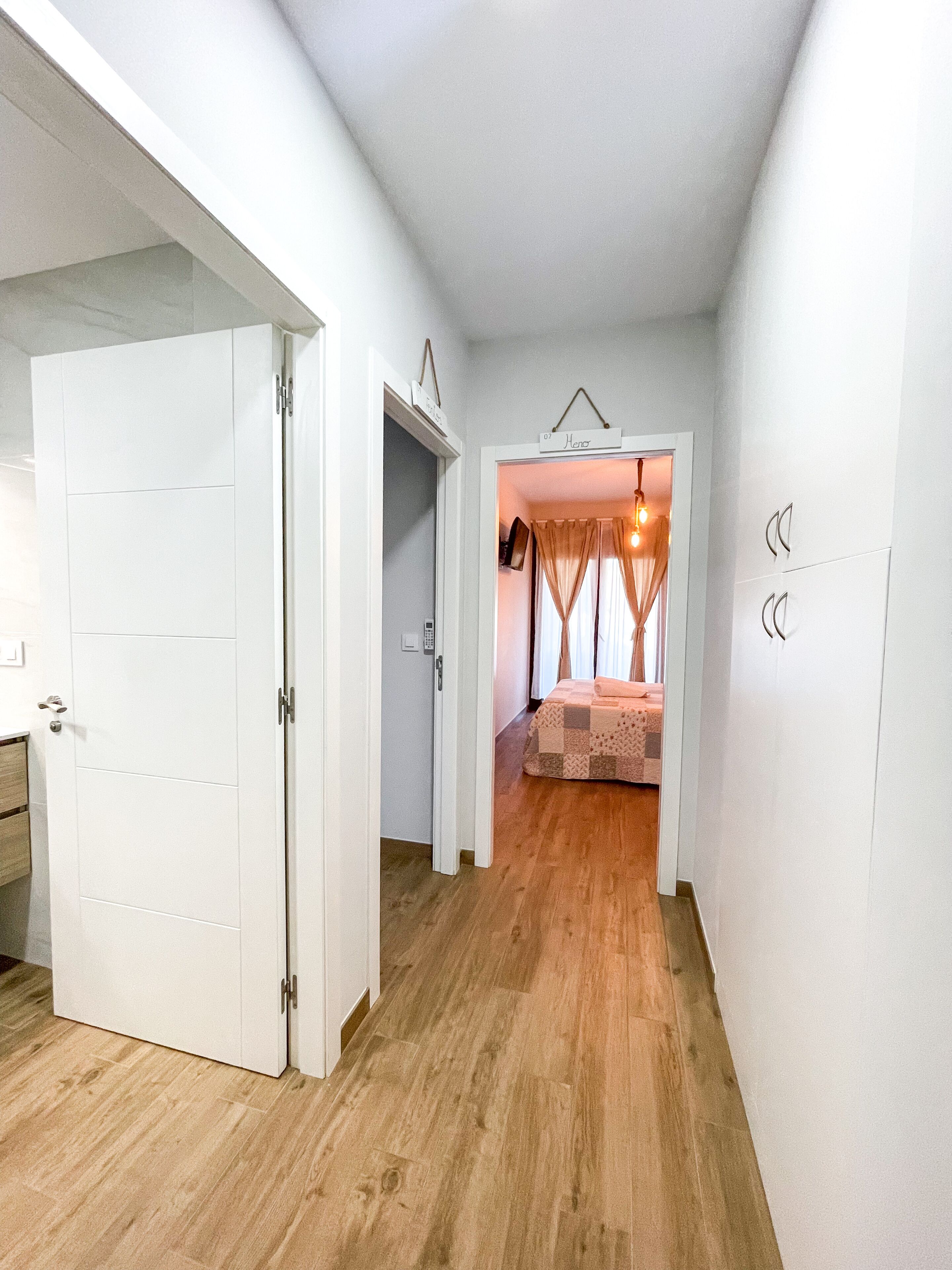 Un couloir menant à une chambre à coucher, qui contient un lit, une porte et une petite table.