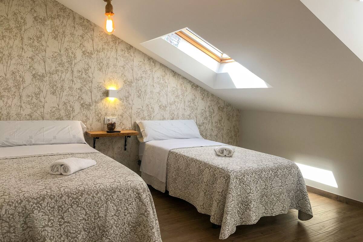 Une chambre avec deux lits, un puits de lumière et un luminaire fixé au mur.