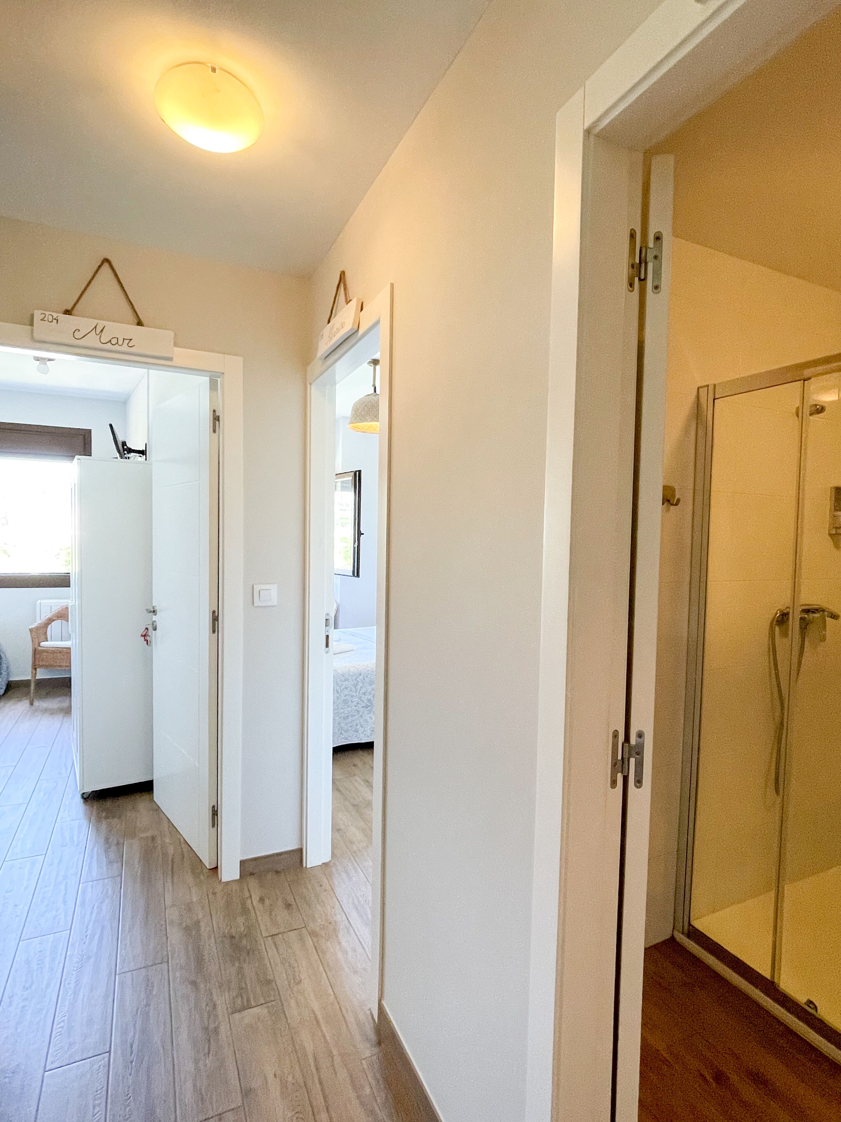 A hotel room with a wooden floor, a glass shower, and a bed with a white bedspread.