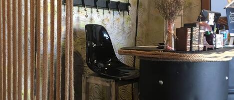A rustic bar area with a wooden chair, a black bar stool, and a black barrel.