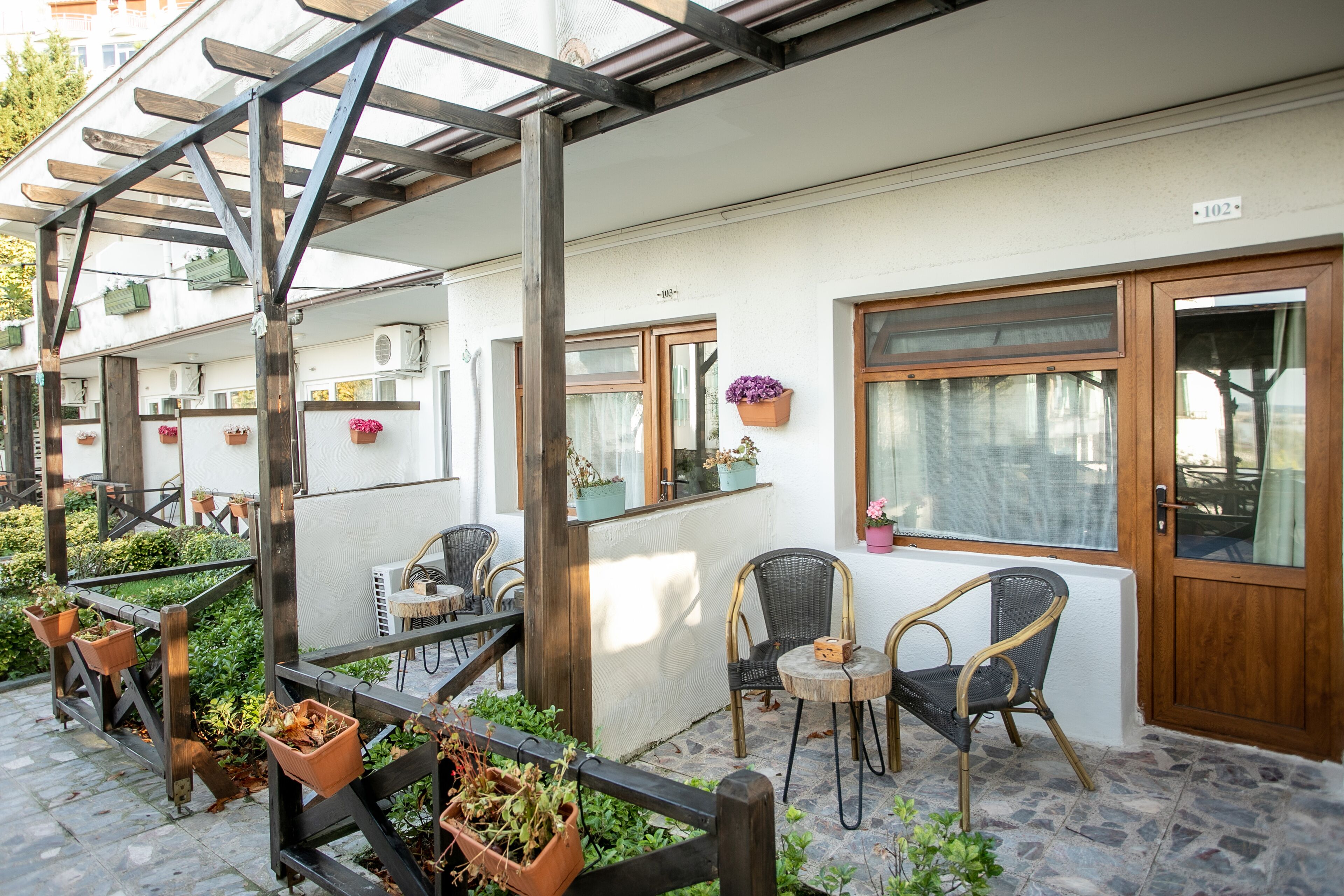 An outdoor seating area with wooden pergola, potted plants, and wicker chairs.