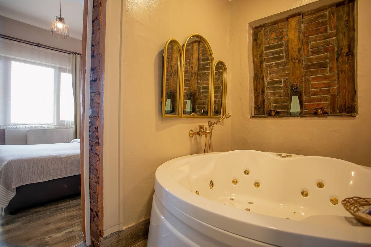 A bathroom with a large bathtub, a mirror, and a window with curtains.