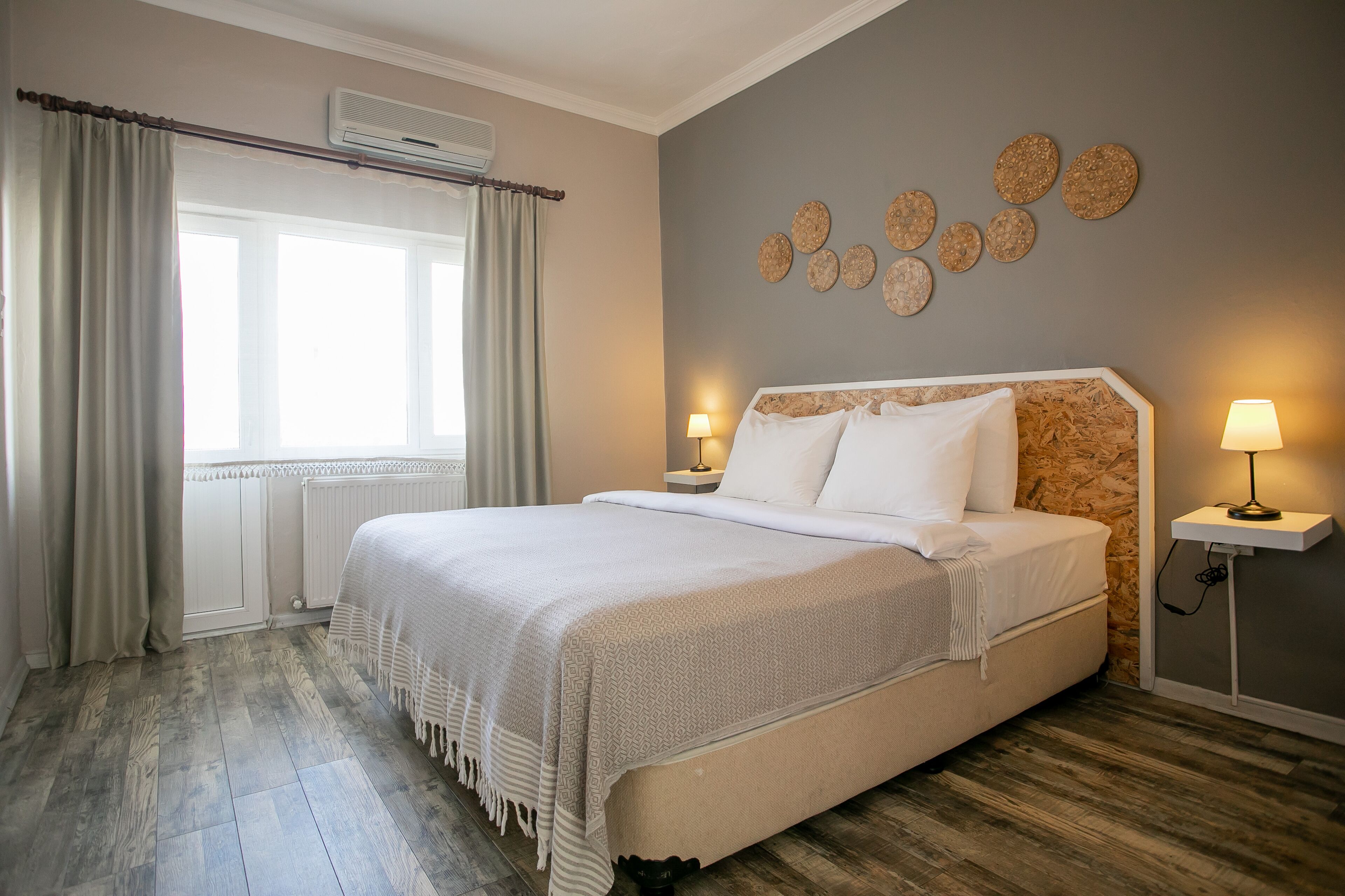 A neatly arranged bedroom with a large bed, two bedside lamps, a radiator, and a window with curtains.