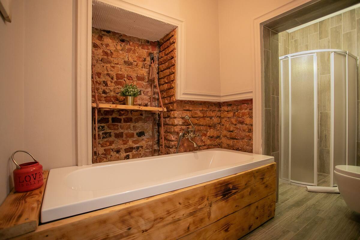 A bathroom with a wooden vanity, a brick wall, a shower enclosure, and a red kettle on the counter.
