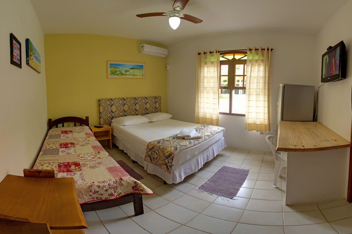 Une chambre à coucher comprenant un lit, un bureau, une chaise, un ventilateur de plafond et une fenêtre avec des rideaux.