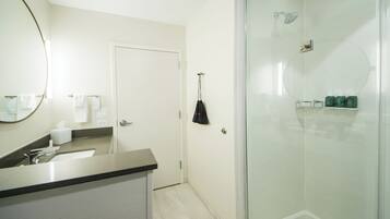 Un baño moderno con cabina de ducha de vidrio, un lavabo con espejo y artículos de aseo en la pared.