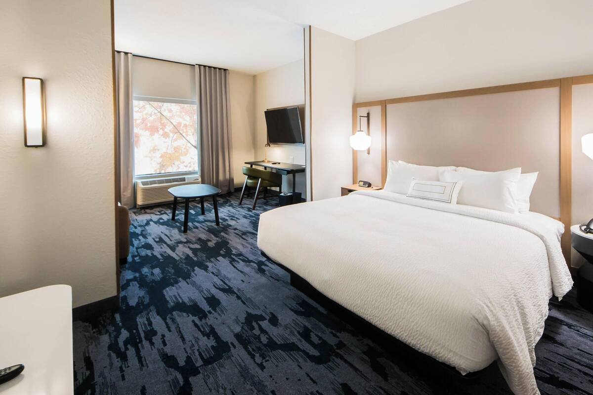 A hotel room with a large bed, a desk with a chair, a television, and a window with curtains.