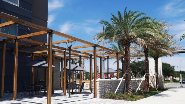 Un espacio al aire libre con pérgolas de madera, asientos de piedra y palmeras.