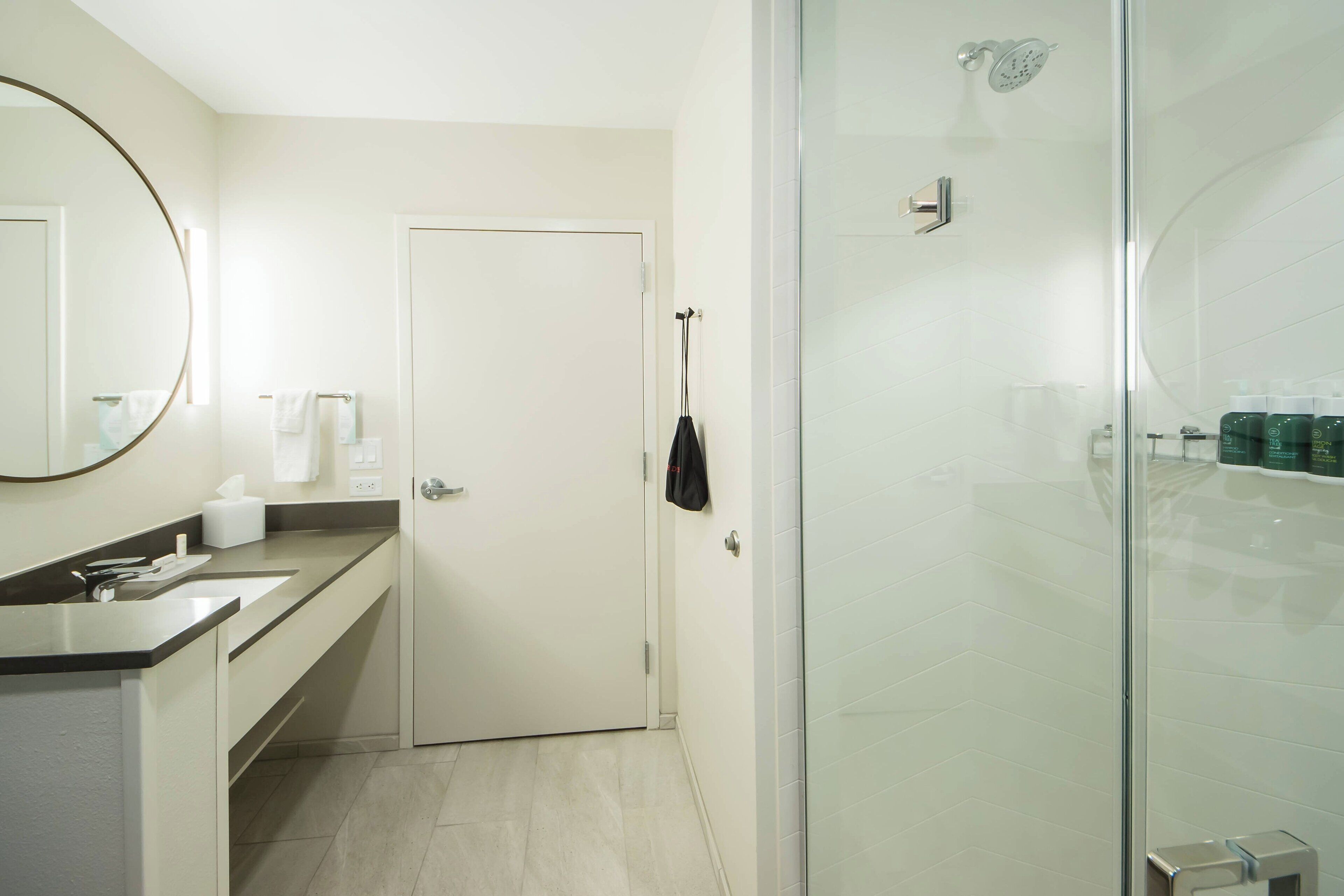 Un baño moderno con cabina de ducha de vidrio, una puerta blanca y un mostrador con un espejo y artículos de aseo.