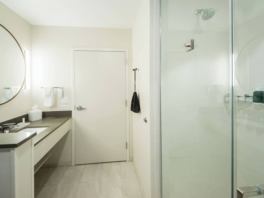 A modern bathroom with a glass shower enclosure, a white door, and a countertop with a mirror and toiletries.