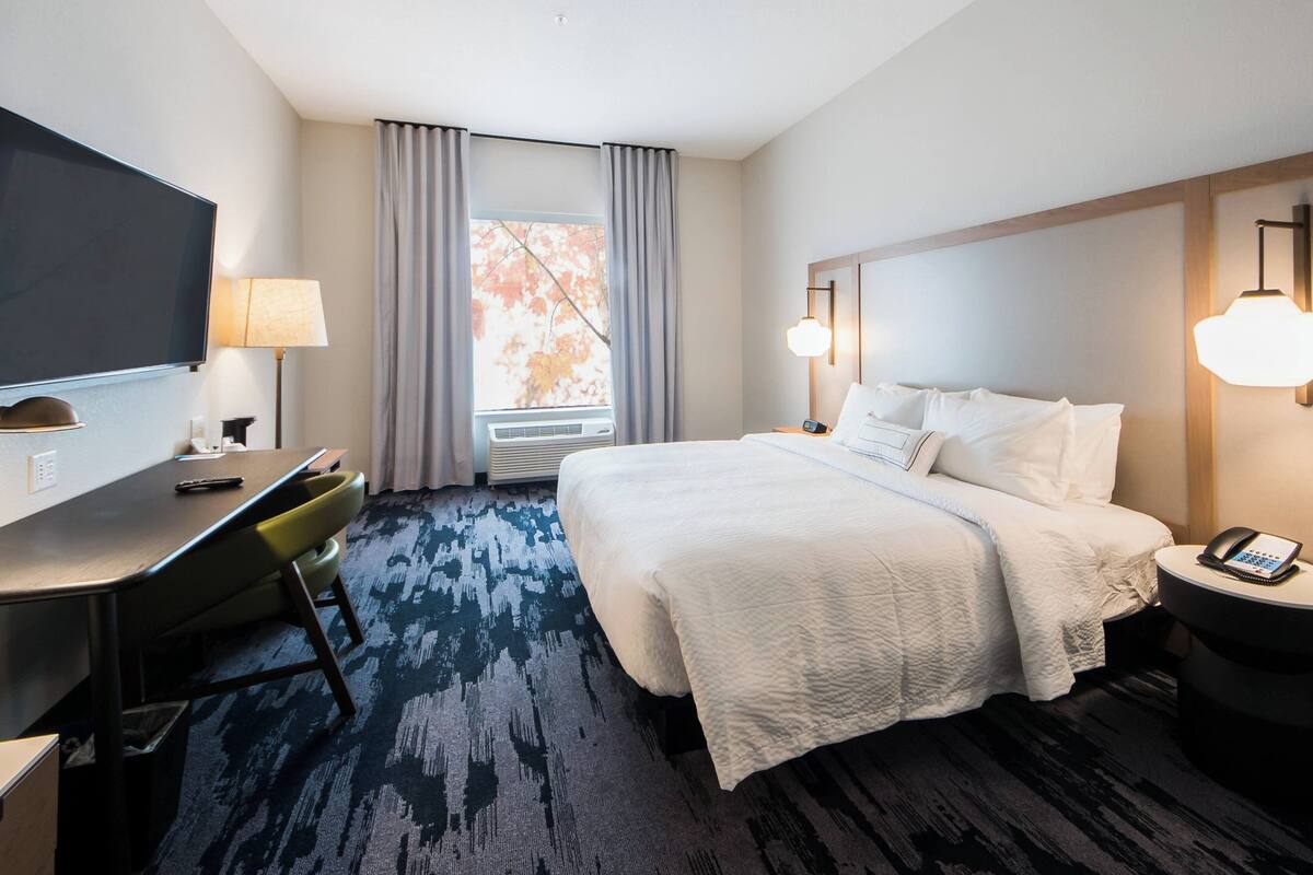 A hotel room with a bed, a desk, a TV, and a window with curtains.