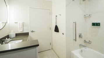 A modern bathroom with a white sink, mirror, and bathtub. There are toiletries on the wall and a towel rack.