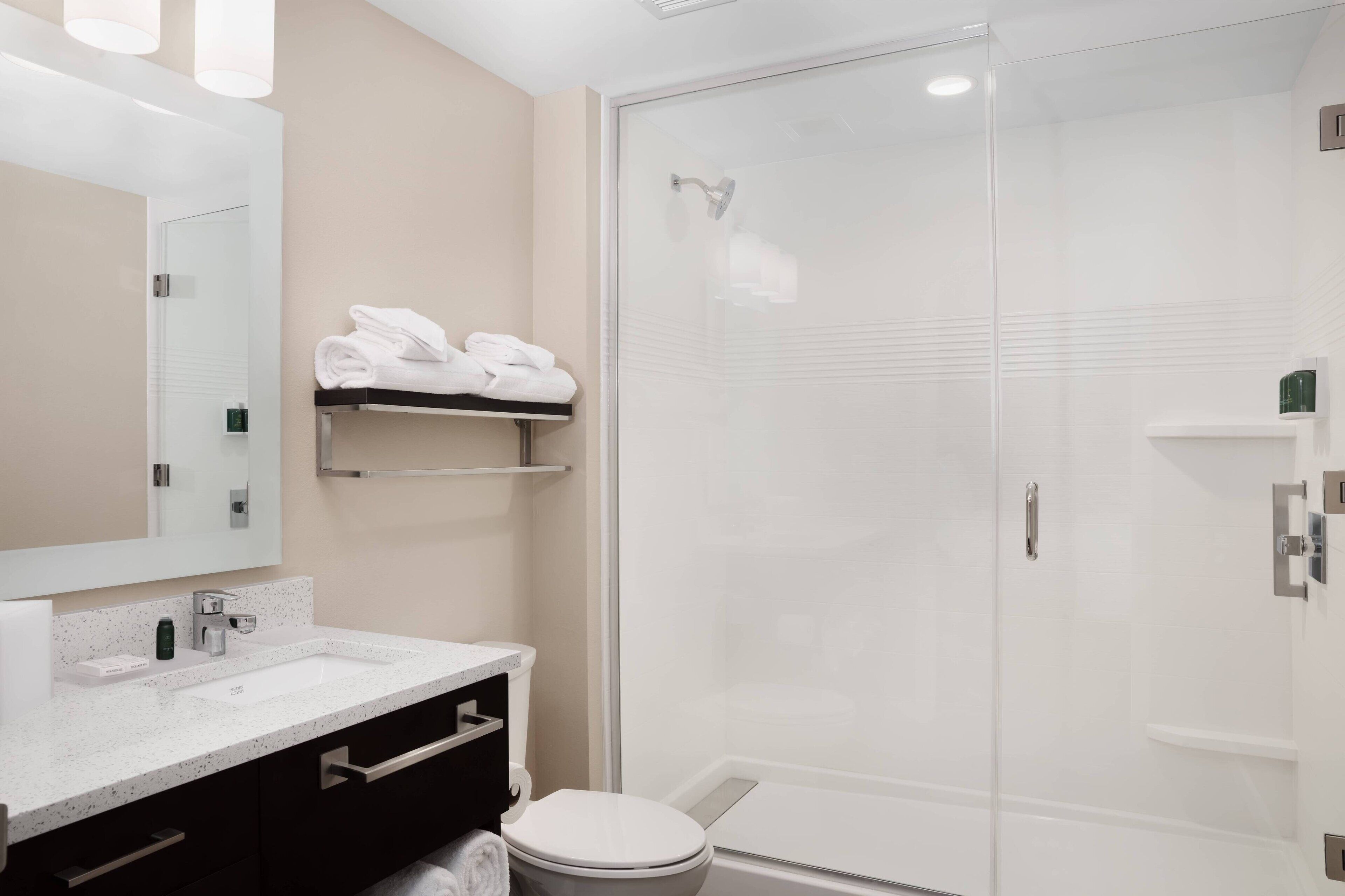Een moderne badkamer met een douchecabine van glas, een witte wastafel en een spiegel erboven.