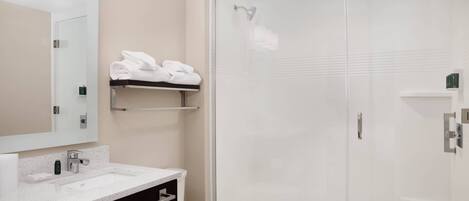 Een moderne badkamer met een douchecabine van glas, een witte wastafel en een spiegel erboven.