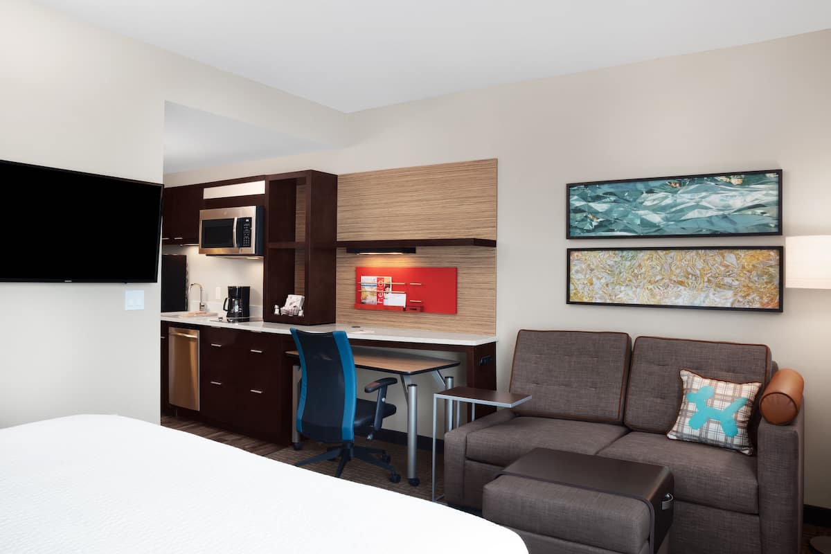 A hotel room with a bed, a desk with a chair, a microwave, a coffee maker, and a TV.