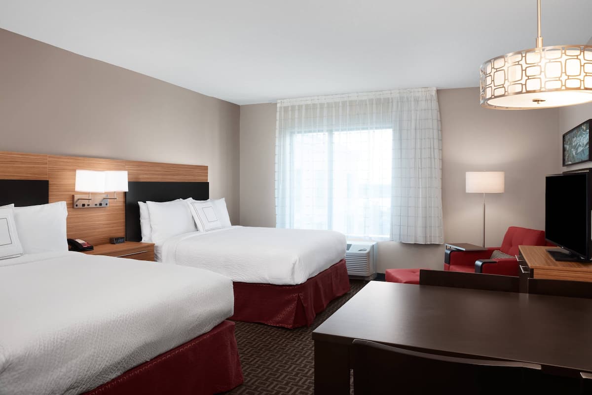 A hotel room with two beds, a desk, a TV, and a large window with curtains.