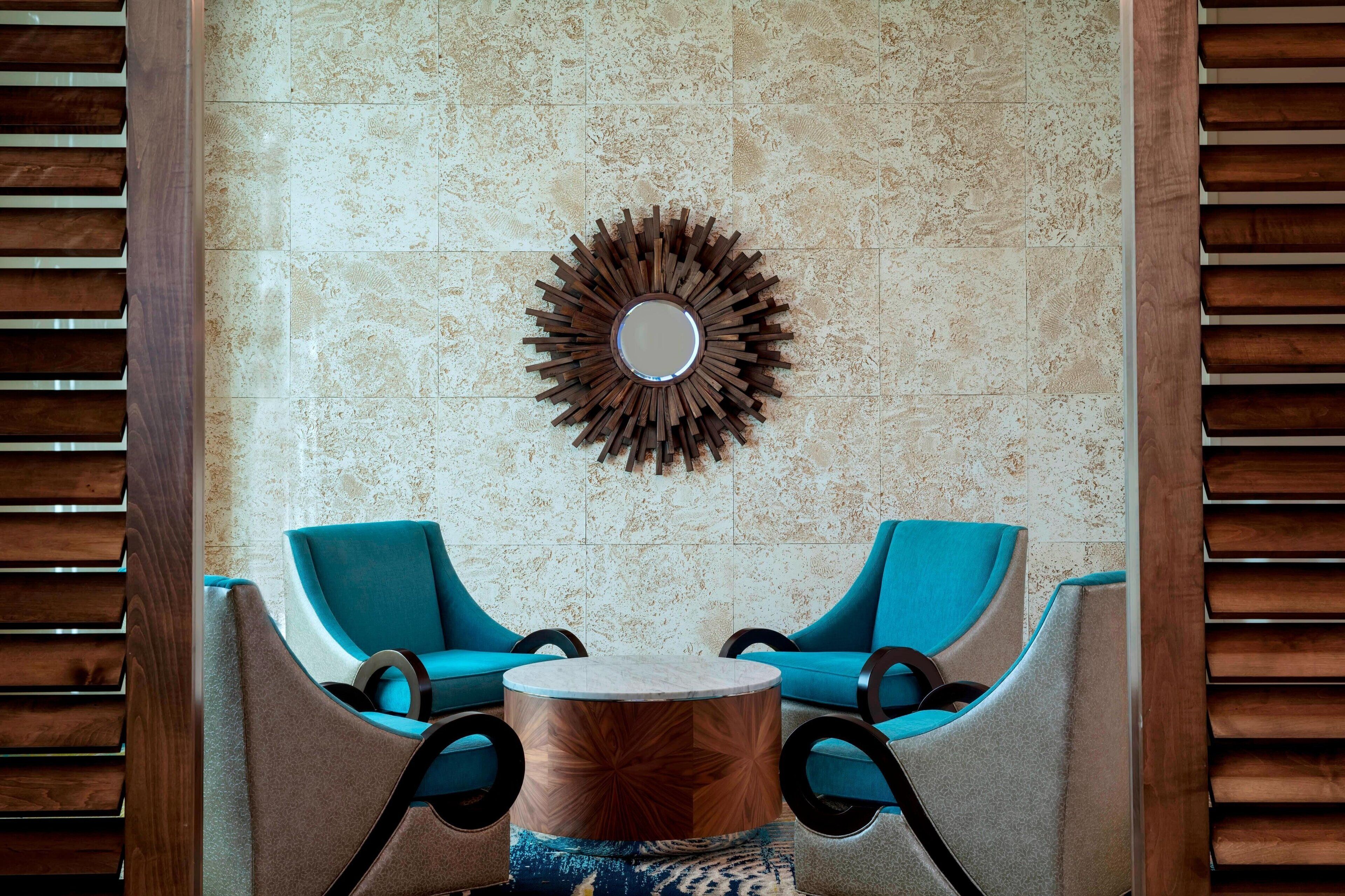 A room with two blue armchairs, a round wooden coffee table, and a decorative mirror on the wall.