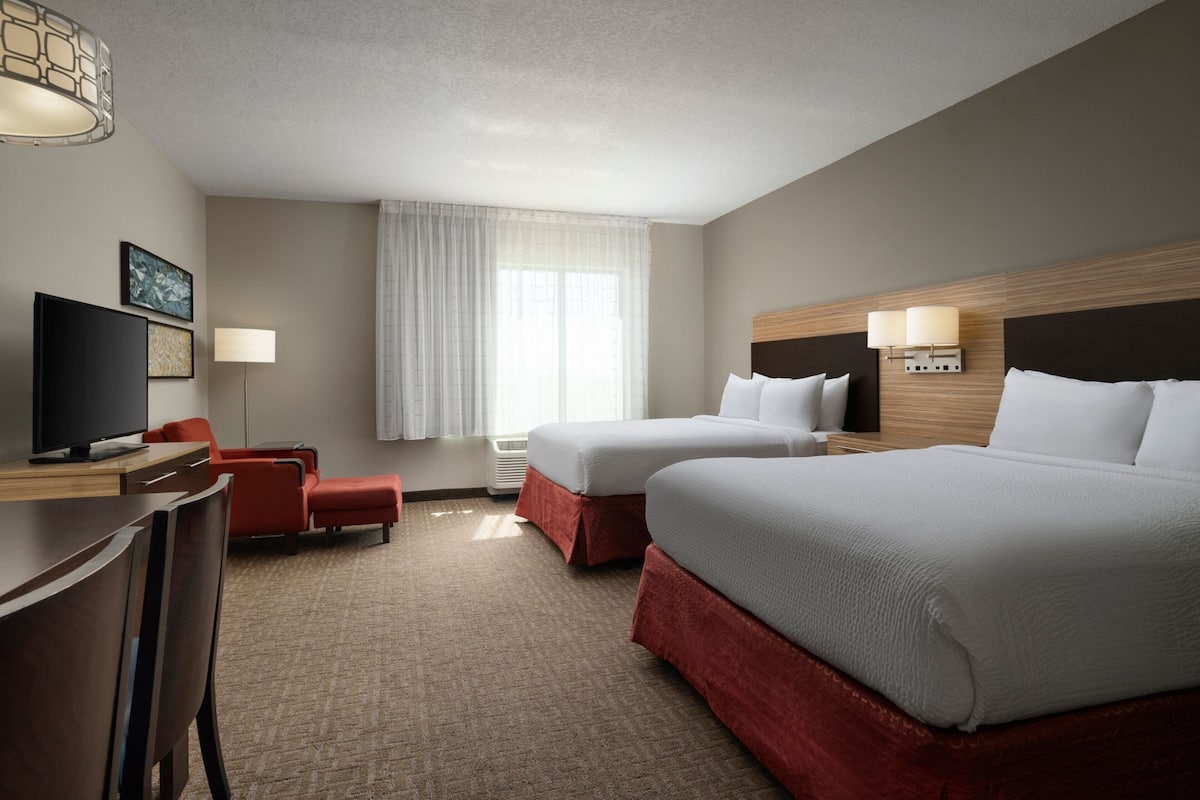 A hotel room with two beds, a desk with a TV, a chair, and a large window with curtains.