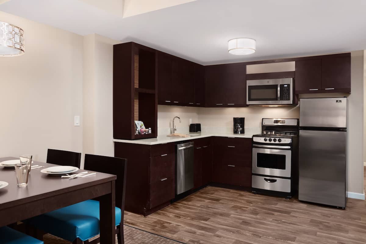 A modern kitchen with dark wooden cabinets, stainless steel appliances, and a dining area with blue chairs.
