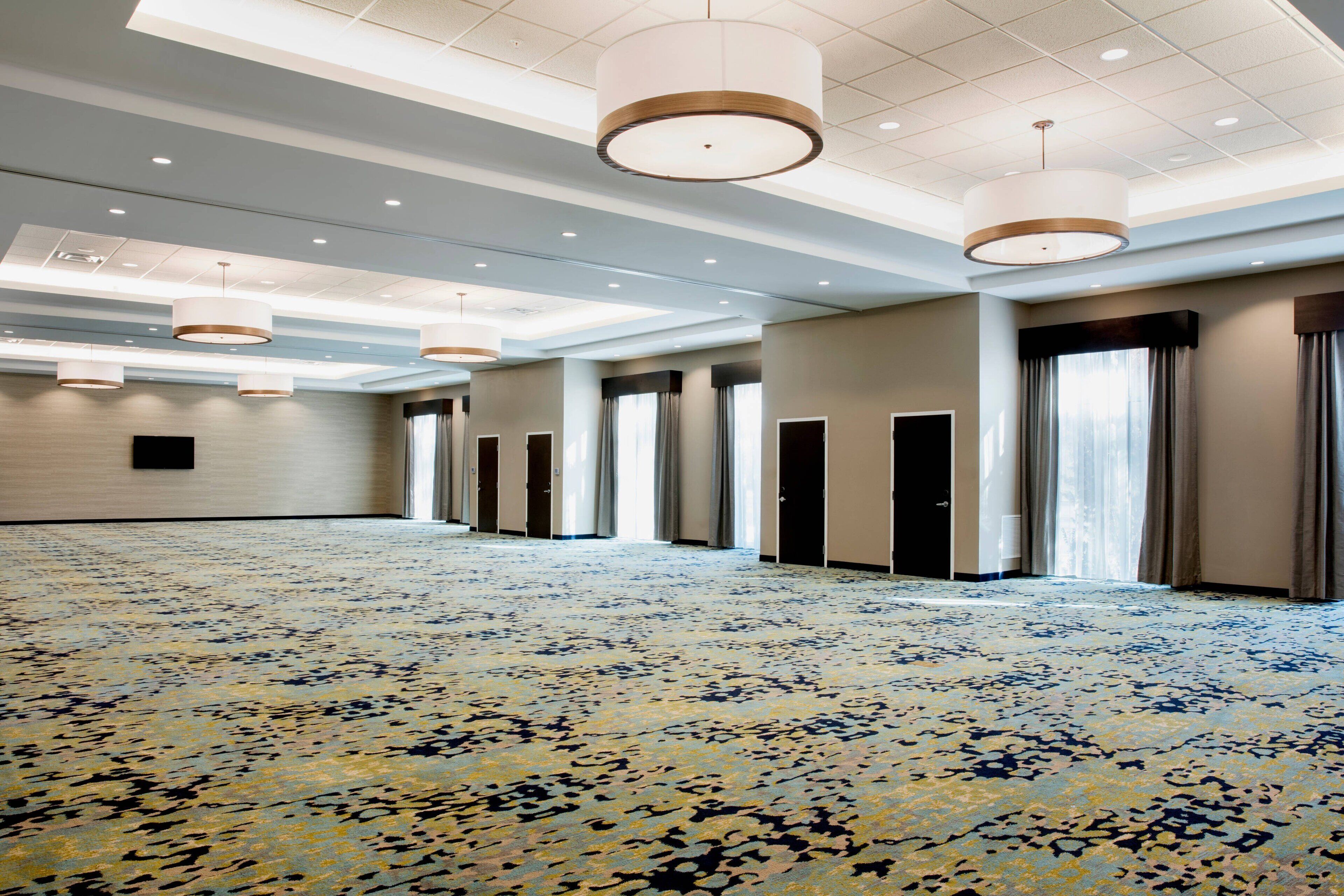 A spacious hotel room with a patterned carpet, multiple doors, and pendant lighting.