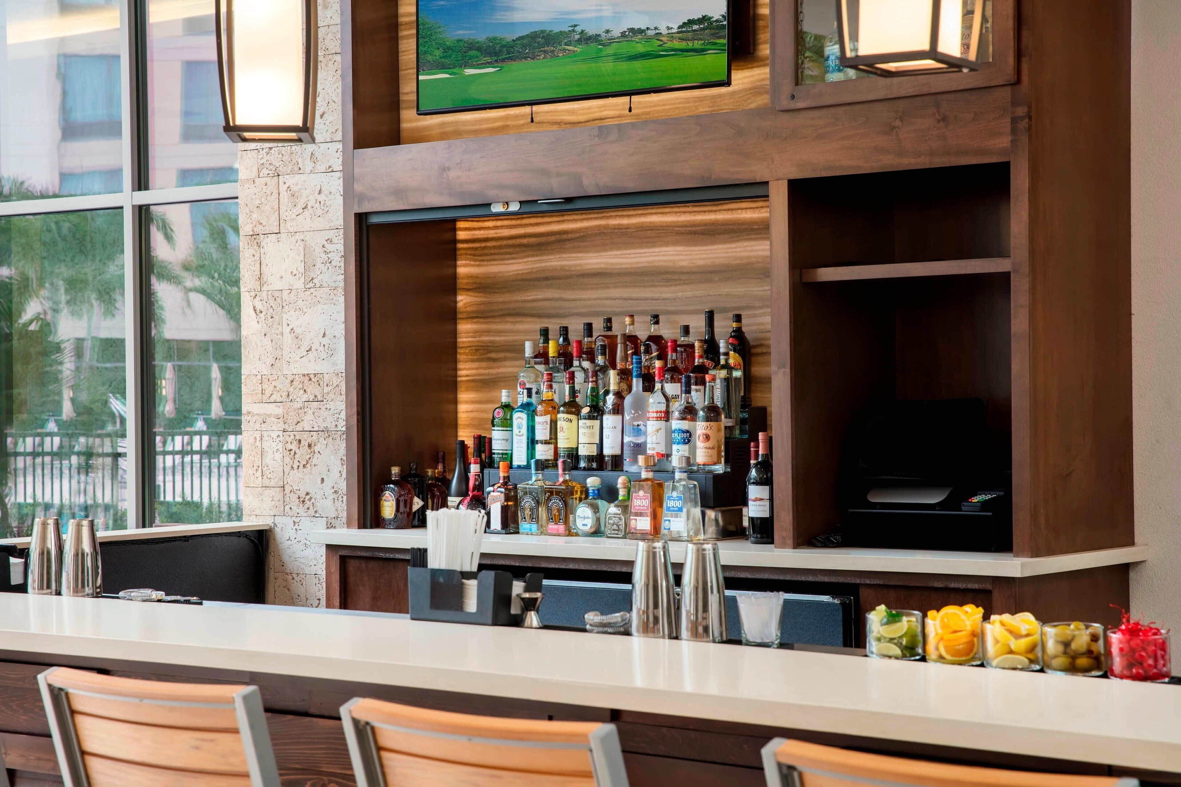 A bar area with a variety of liquor bottles, a television mounted above the bar, and a view of a golf course through large windows.