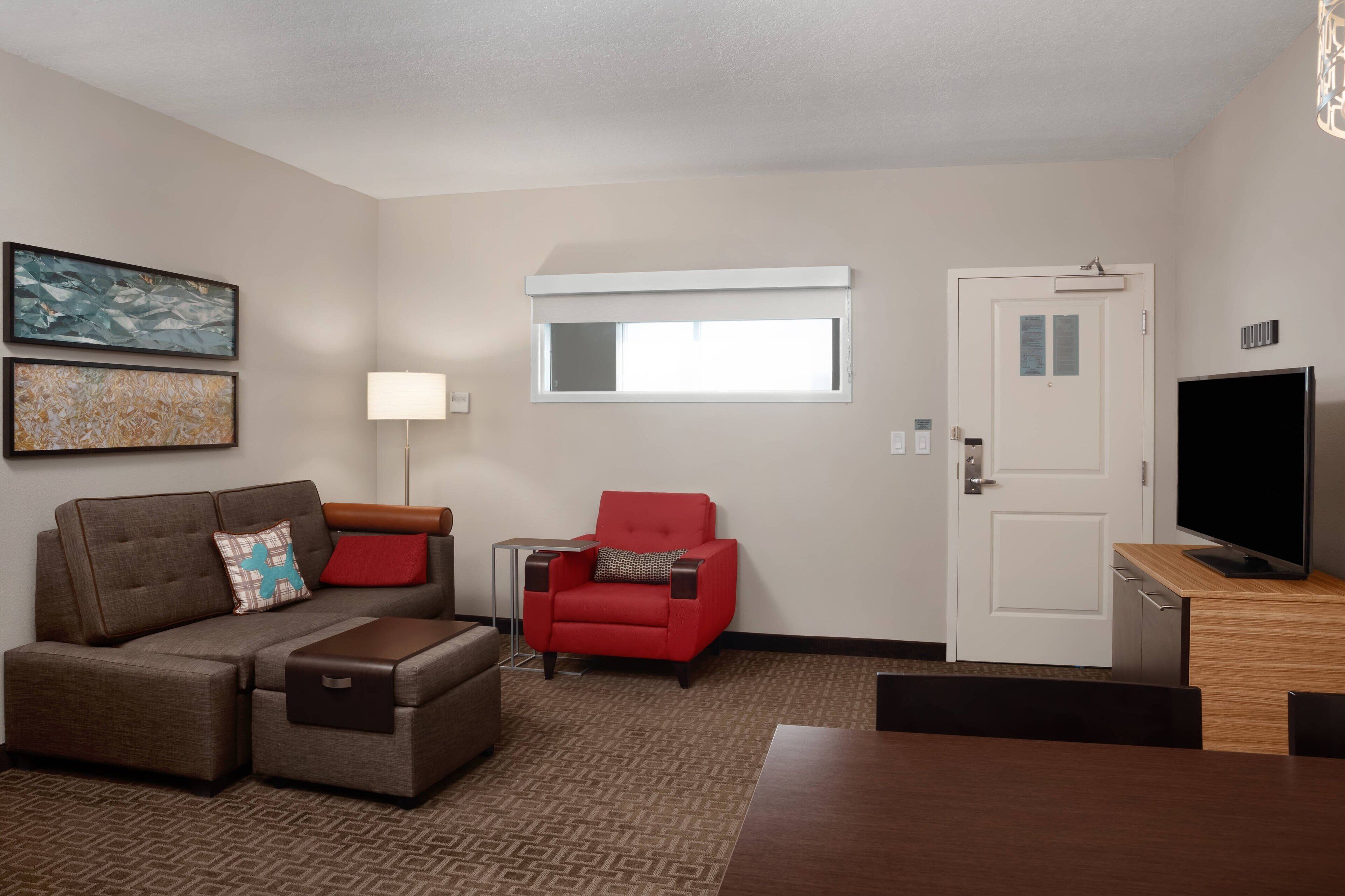 A hotel room with a sofa, armchair, TV, and a door.