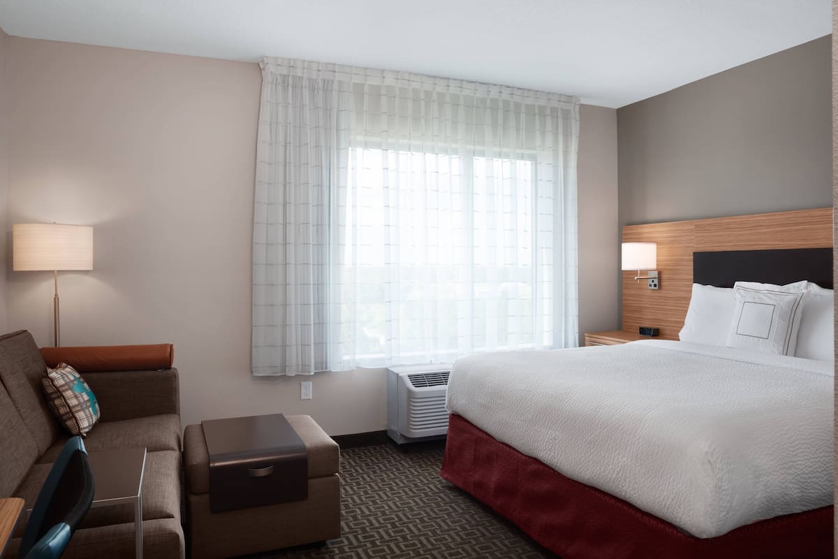 A hotel room with a bed, a desk, a chair, a sofa, a lamp, and a window with curtains.