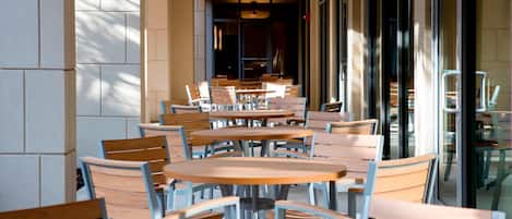 Filas de mesas y sillas de madera en un café con ventanas amplias y un ventilador de techo.