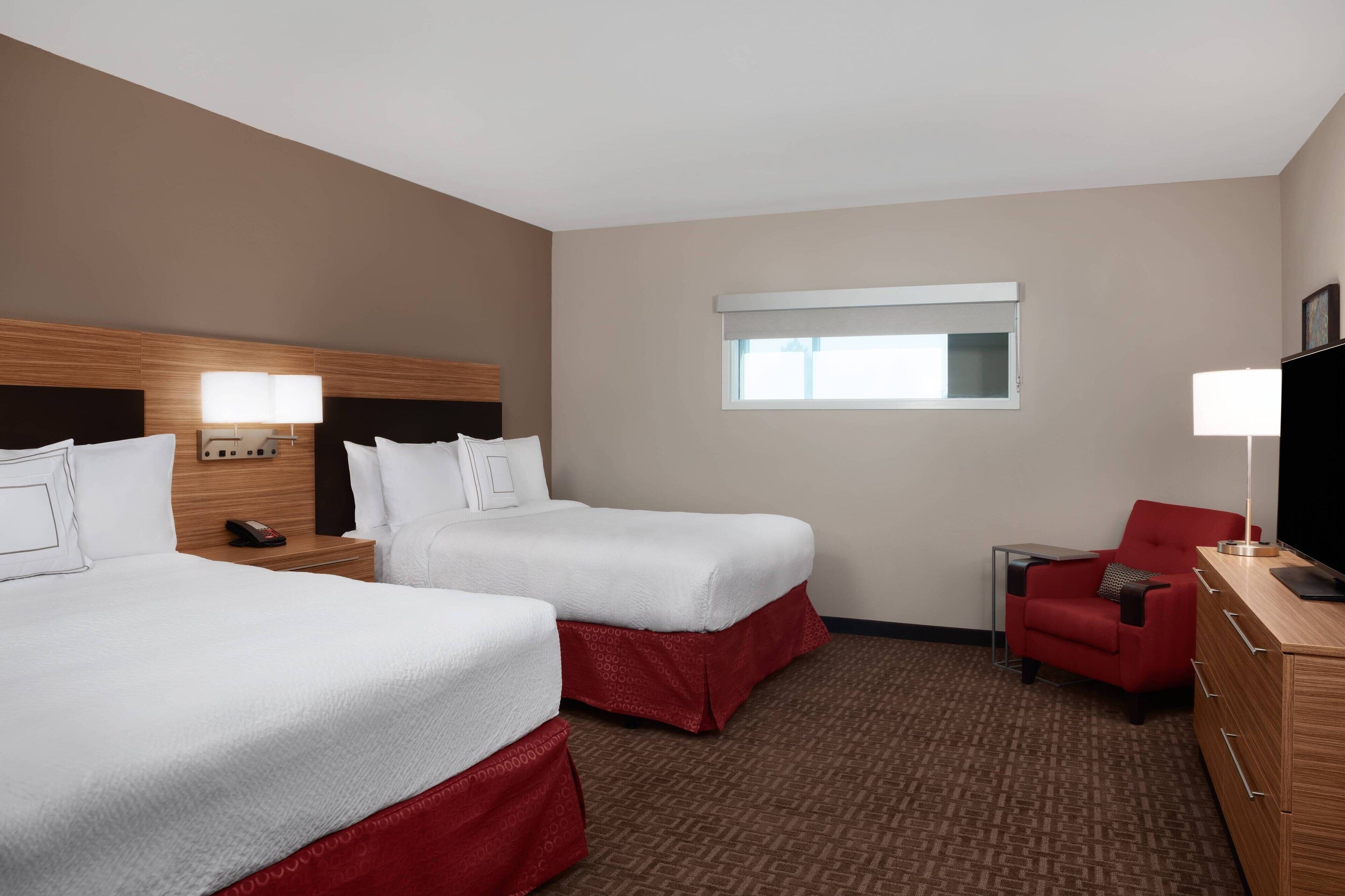 A hotel room with two beds, a TV, a desk, and a chair.