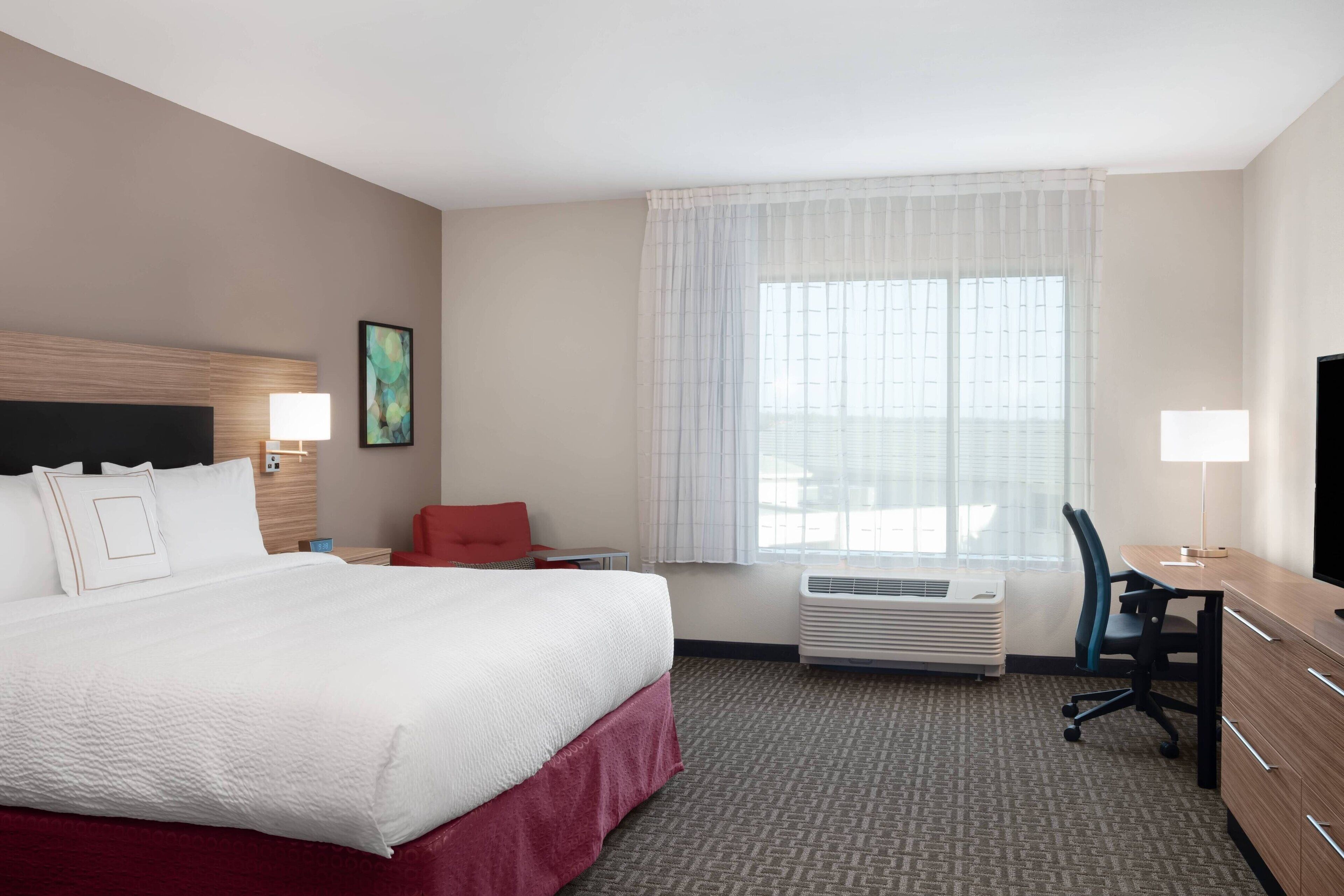 A hotel room with a large bed, a desk, a chair, a TV, and a window with curtains.