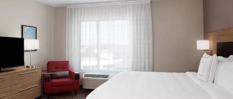 Habitación de hotel con cama, sillón rojo, televisor, escritorio y ventana con cortinas de gasa.
