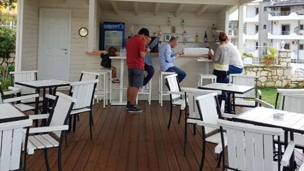 An outdoor patio area with white tables and chairs, a bar area, and a wooden deck.