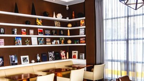 A modern library with a high ceiling, bookshelves, a dining area, and a large window.