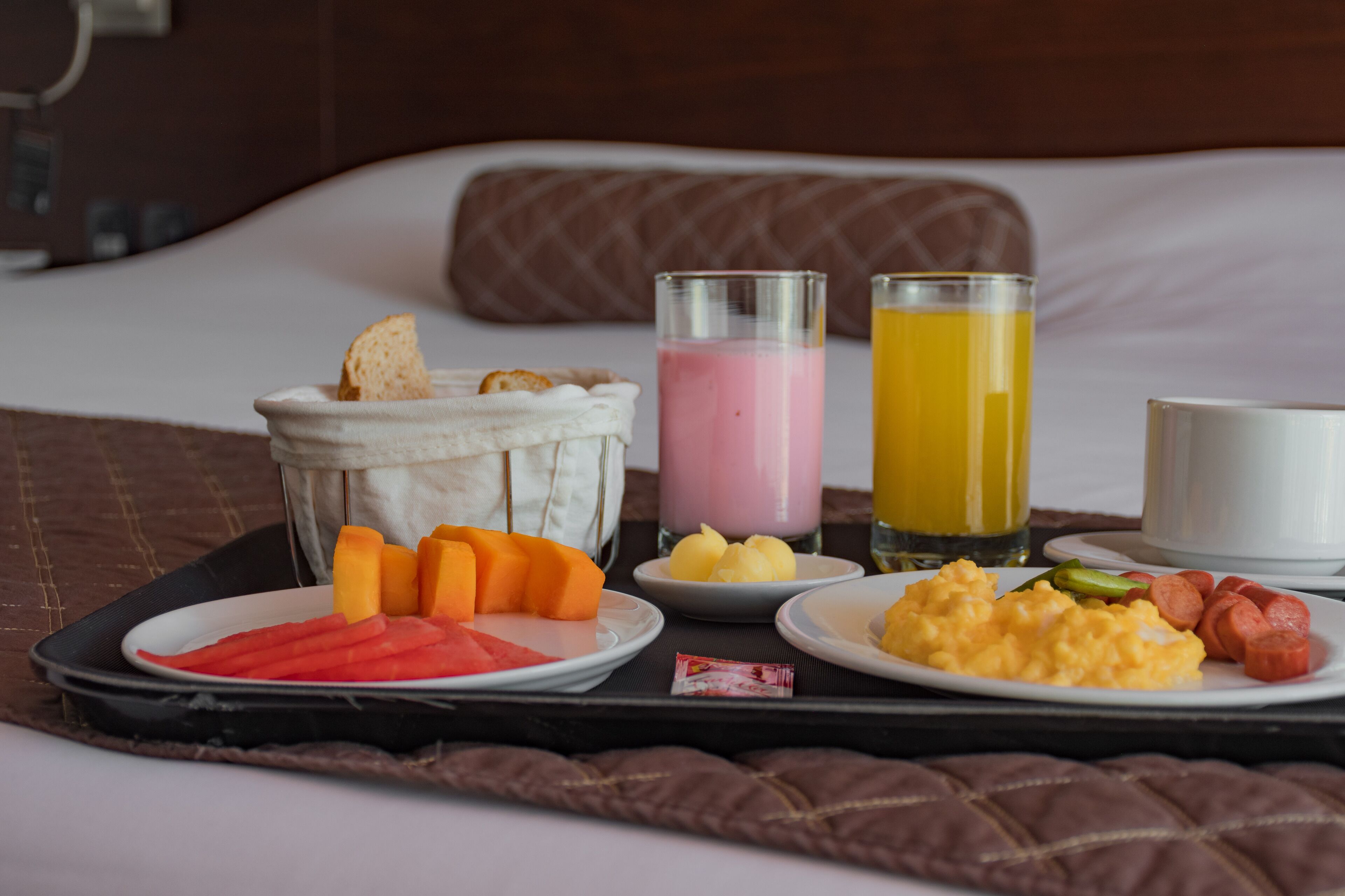 Una bandeja de desayuno con diversos alimentos y bebidas sobre una cama.