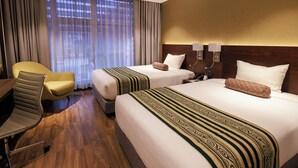 A hotel room with two beds, a desk, a chair, and a large window with curtains.